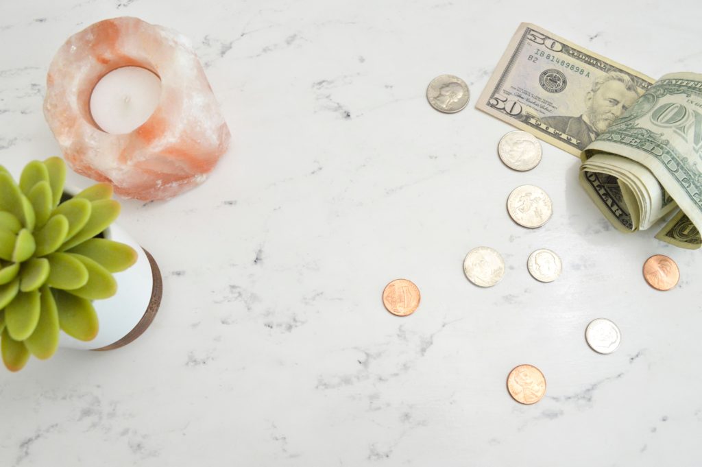 Flatlay of money, a candle, and a succulent on a marble surface.