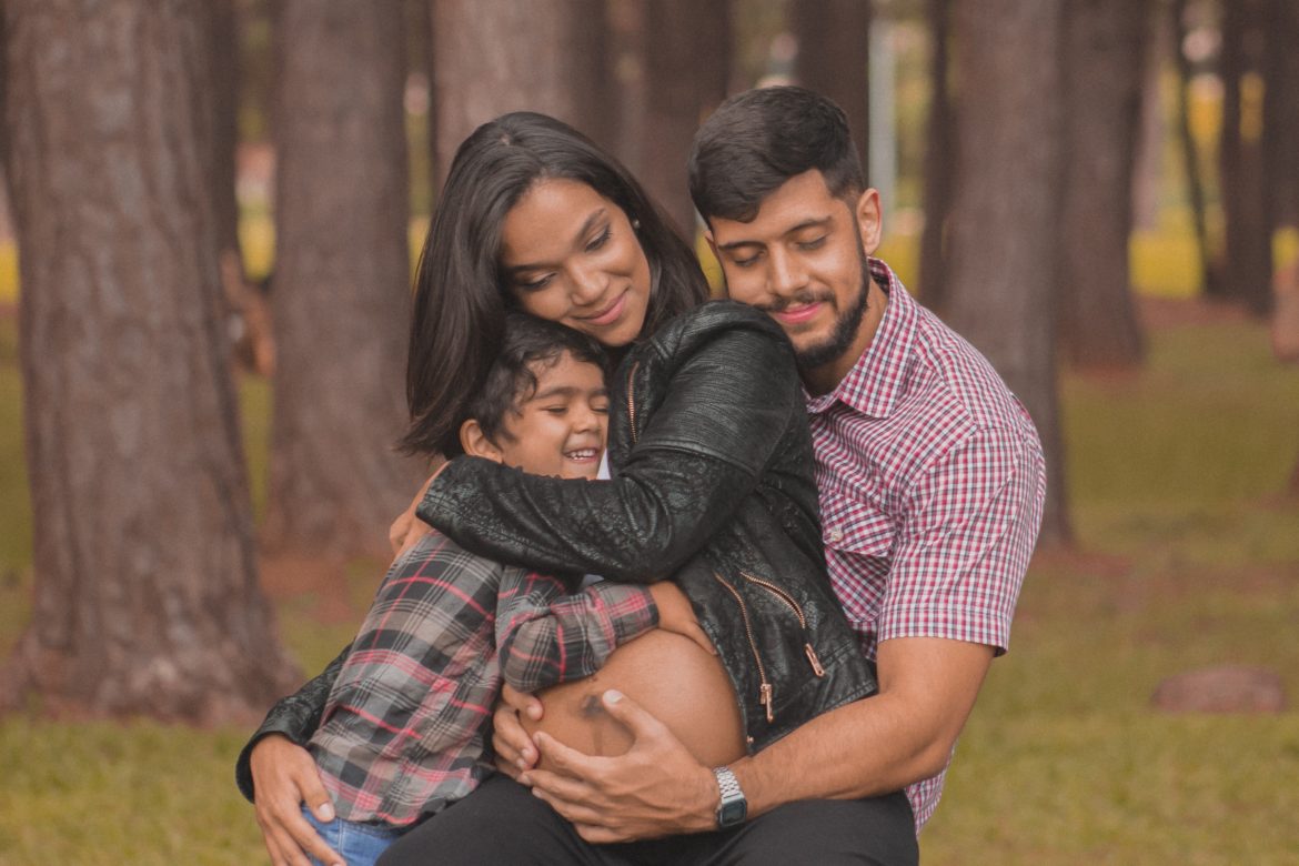 A pregnant woman hugged by her son and husband.