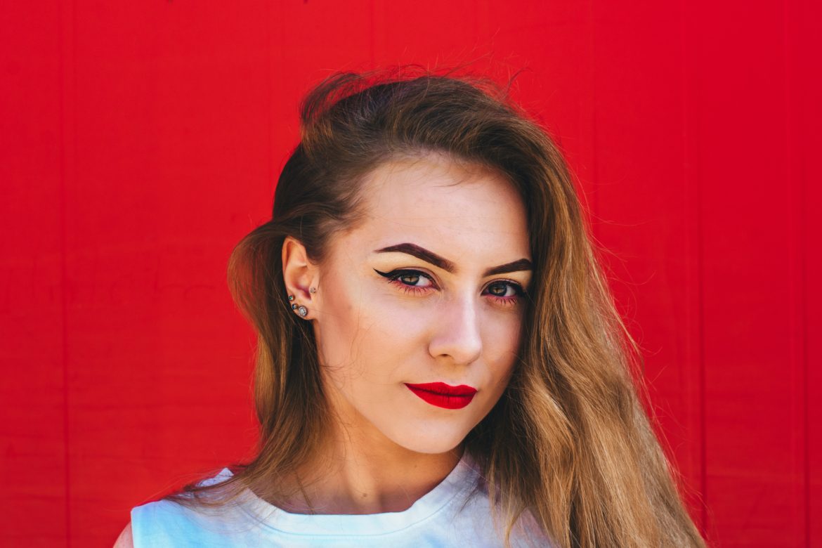 Woman wearing bold makeup and standing in front of a red background.