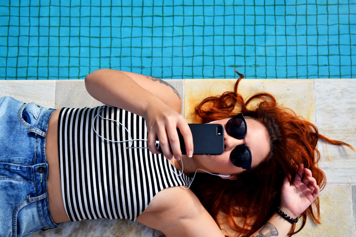 Woman lying next to a pool while looking at her phone.