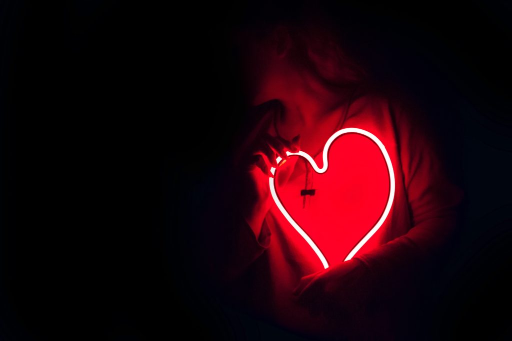 Woman holding a large neon heart towards her chest.